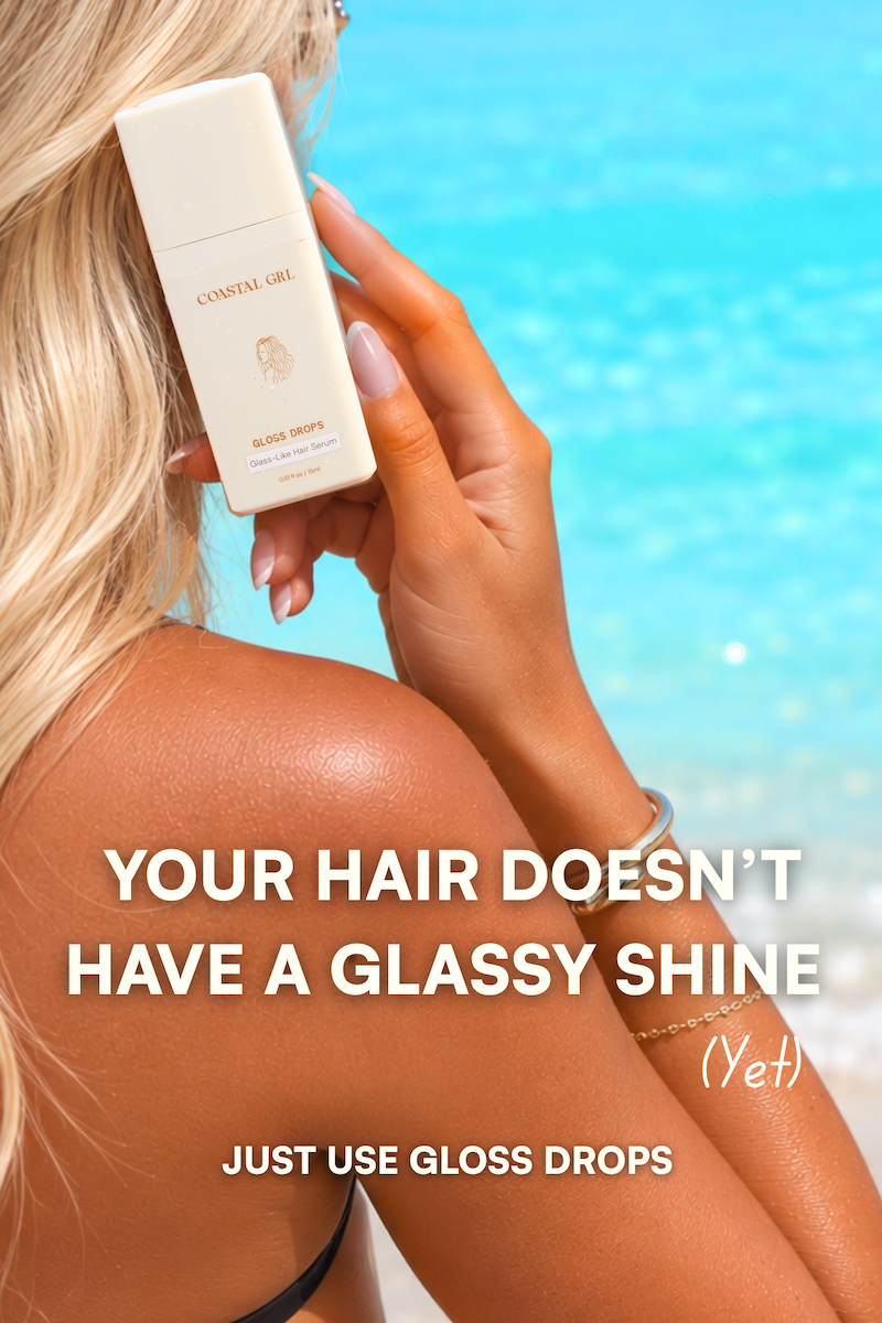 Woman with blonde hair holding Coastal GRL Gloss Drops glass-like hair serum against a turquoise ocean