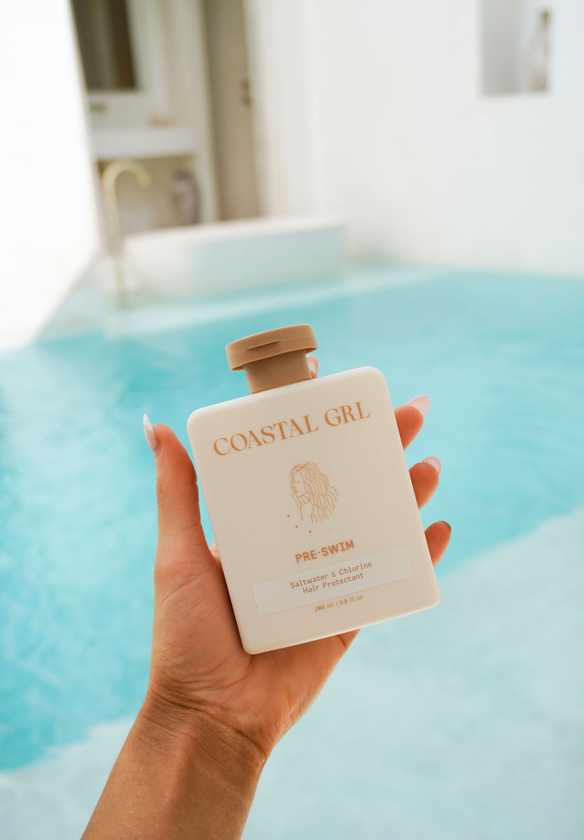 Hand holding the Coastal GRL Pre-Swim hair protector bottle beside a pool