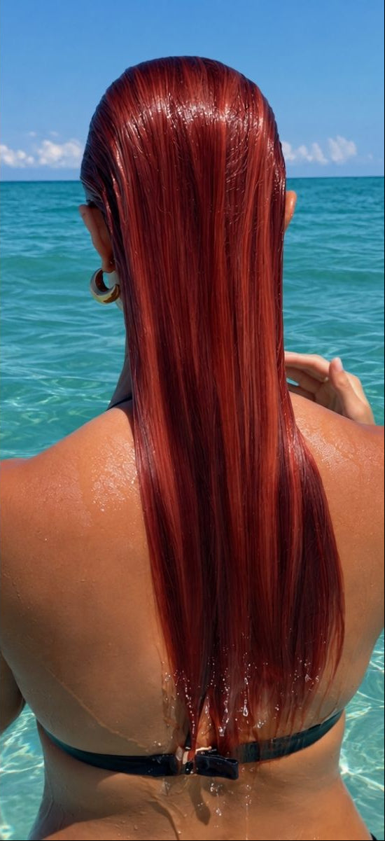 Back view of a woman in clear turquoise water with long, sleek, wet red hair slicked straight