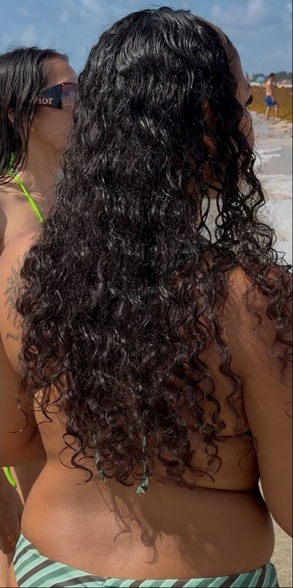 Back view of a woman at the beach with long, dark, defined curly hair falling past her shoulders