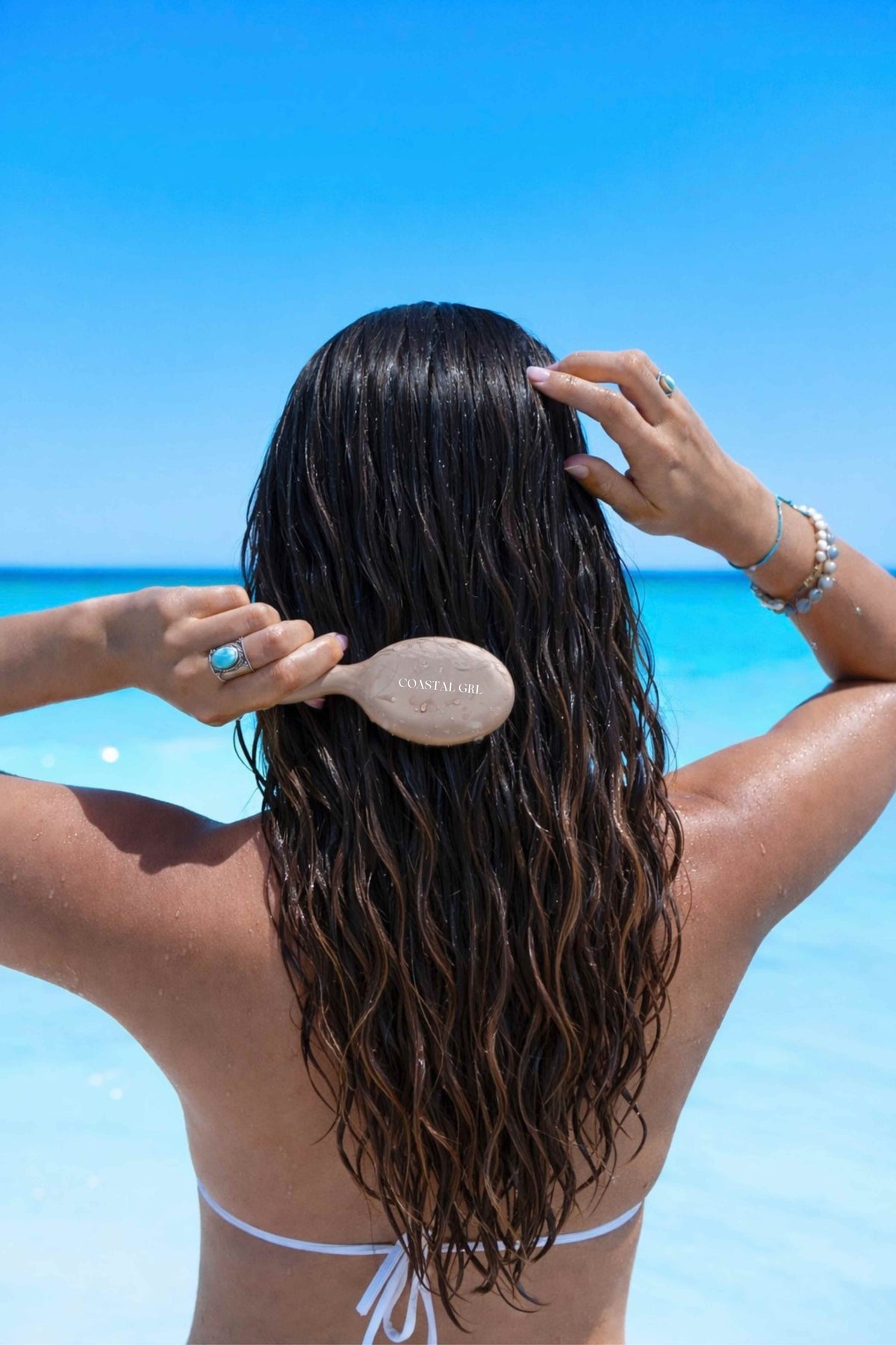 Person brushing their wet hair on a beach with clear blue sky